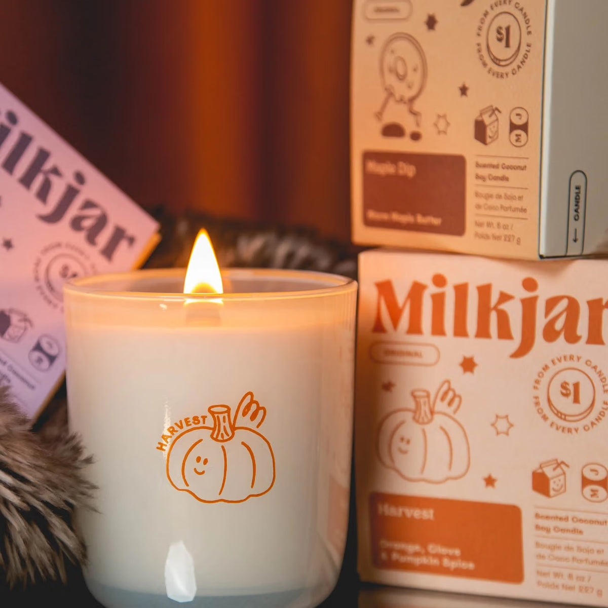 Lit Milk Jar candle beside branded boxes