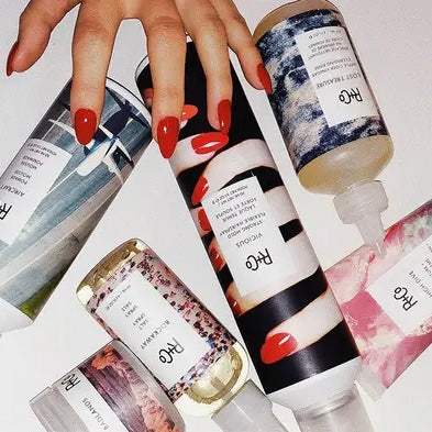 Hand with red nails holding assorted R+Co haircare products