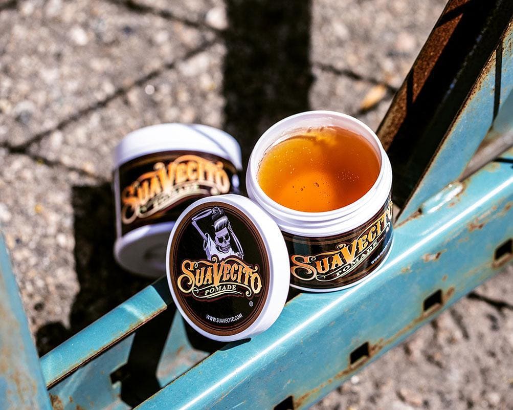 Open Suavecito Original Hold Pomade jar and lid on blue surface