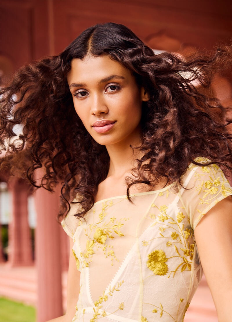 Woman wearing a light-colored saree with floral patterns in an outdoor setting KEVIN.MURPHY MOTION.LOTION lightweight curl enhancing lotion for fine hair