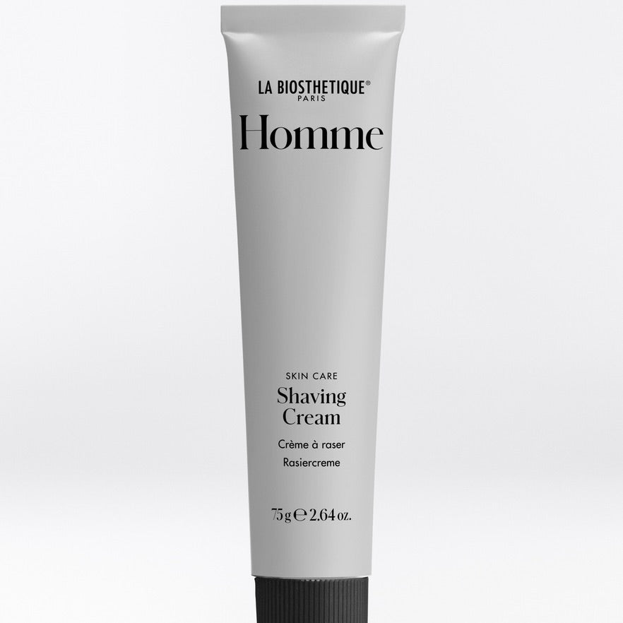 A white squeeze tube of La Biothetique Homme Shaving Cream with black text, set against a light gray gradient background.