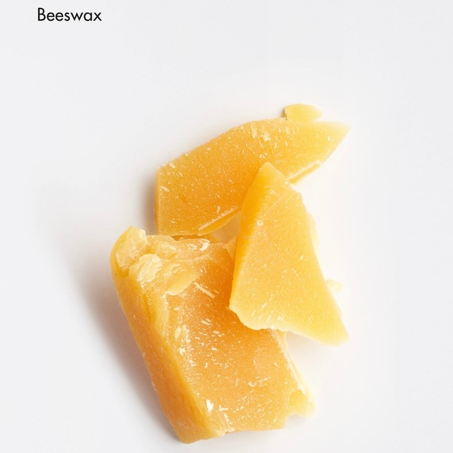Three irregular pieces of pale golden yellow beeswax solidifying on a plain white background, with the word 'Beeswax' printed in the top-left corner.