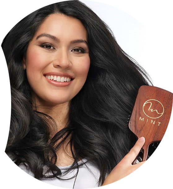 Woman with long black hair holding a wooden comb with 'Mint' branding.