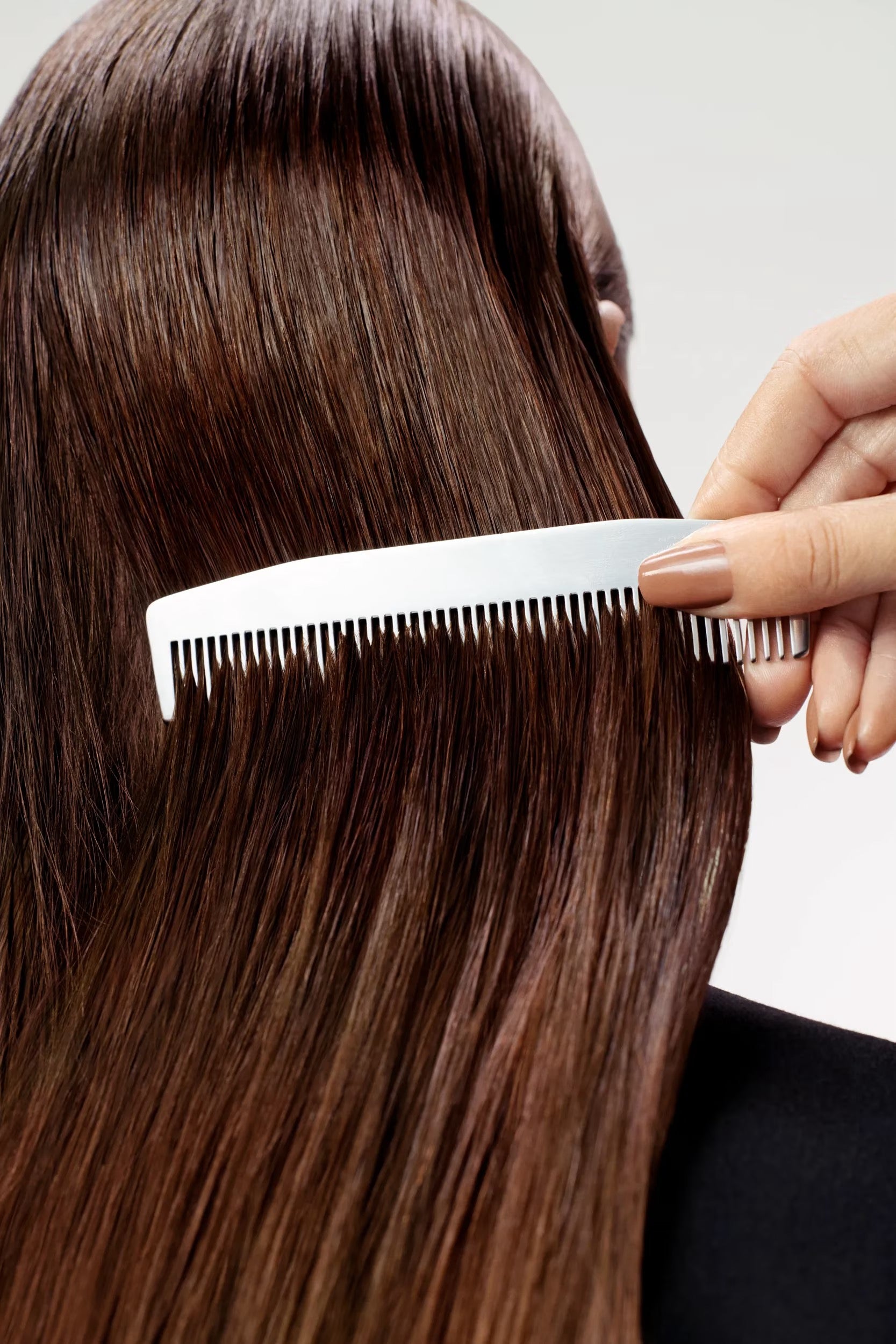 Person combing their straight brown hair with a white comb on a light gray background