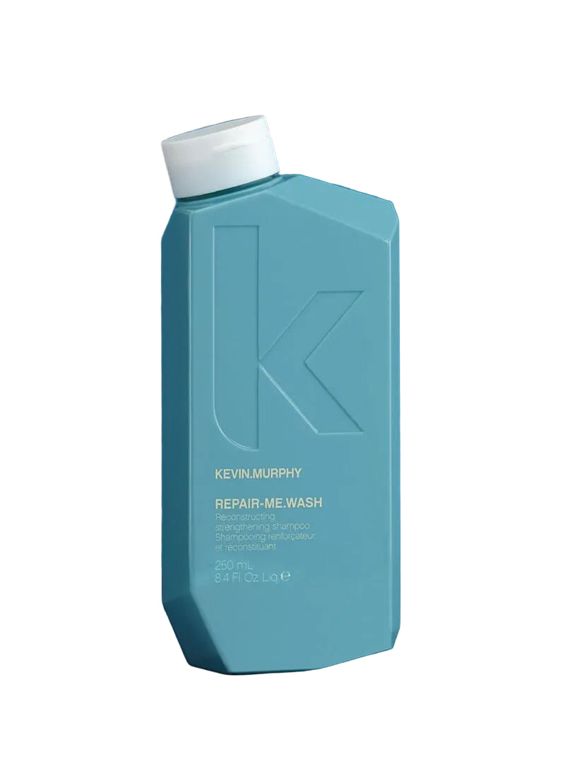 Kevin Murphy Repair-Me Wash shampoo bottle in a muted teal-blue color with a white cap, standing on a dark navy surface against a solid blue background.