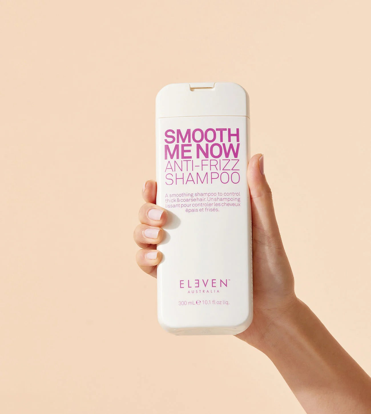 Hand holding a bottle of 'Smooth Me Now Anti-Frizz Shampoo' by Elvien against a beige background