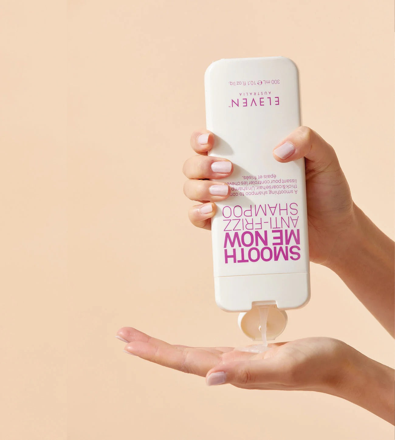 Hand holding a bottle of 'Eleven' shampoo with pump, against a beige background