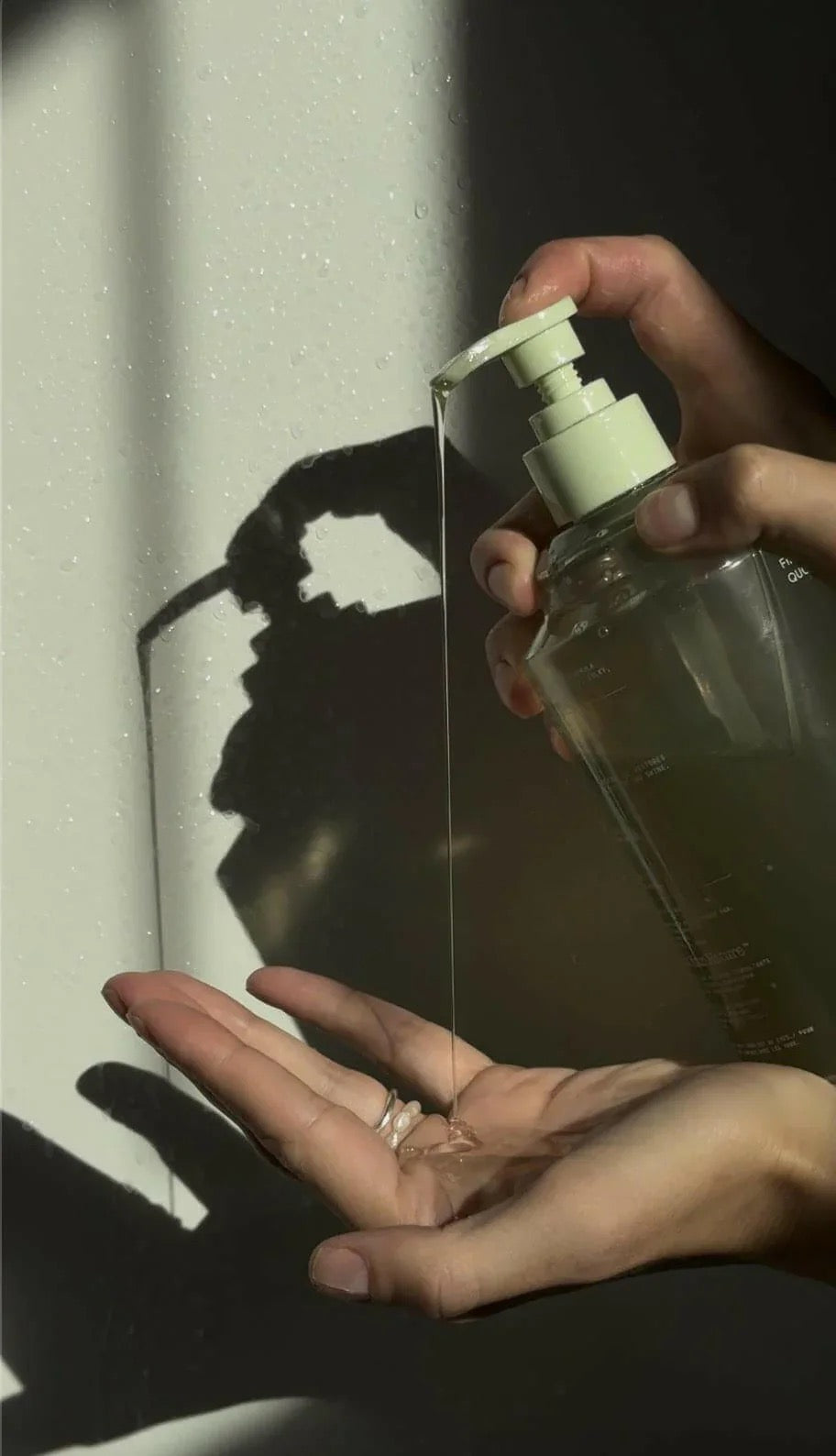Hand holding a clear spray bottle with a white pump against a light background