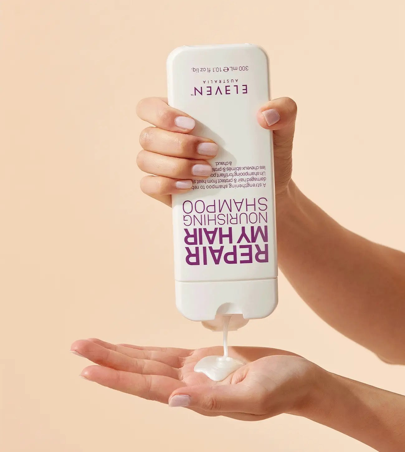 Hand holding a bottle of Elven Nourishing Shampoo with shampoo being dispensed onto a palm against a beige background
