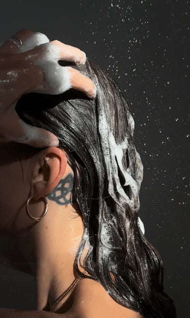 Person applying shampoo to their hair with a dark background