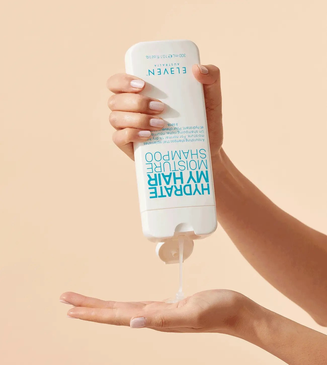 Hand holding a bottle of shampoo with visible shampoo being dispensed onto the palm against a beige background