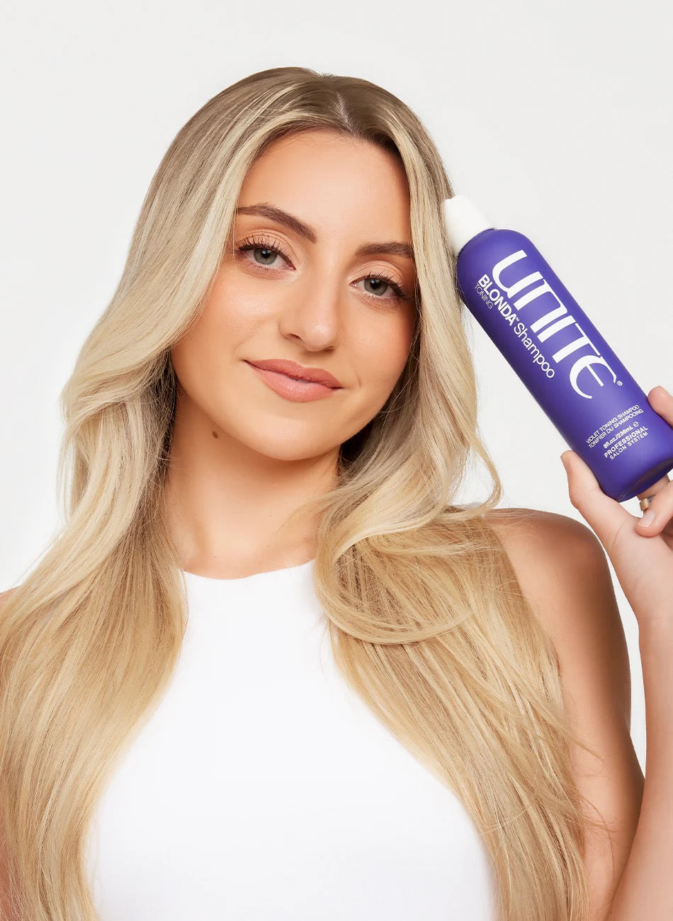 Woman holding a purple shampoo bottle with visible branding against a plain background