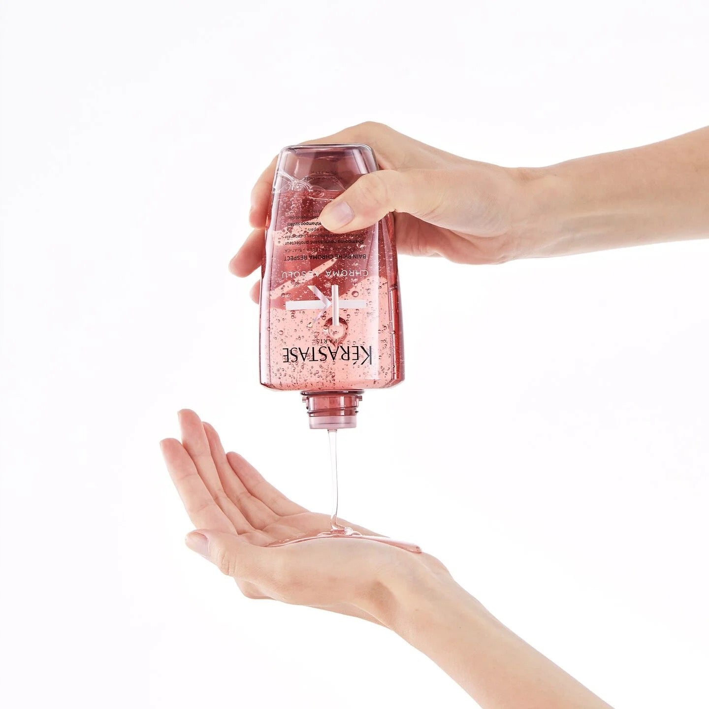 Hand holding a pink Kérastase Chroma Absolu Bain Riche Chroma Respect Shampoo for colour-treated hair in Canada at Curious Salons 
 bottle with product being dispensed onto another hand against a white background