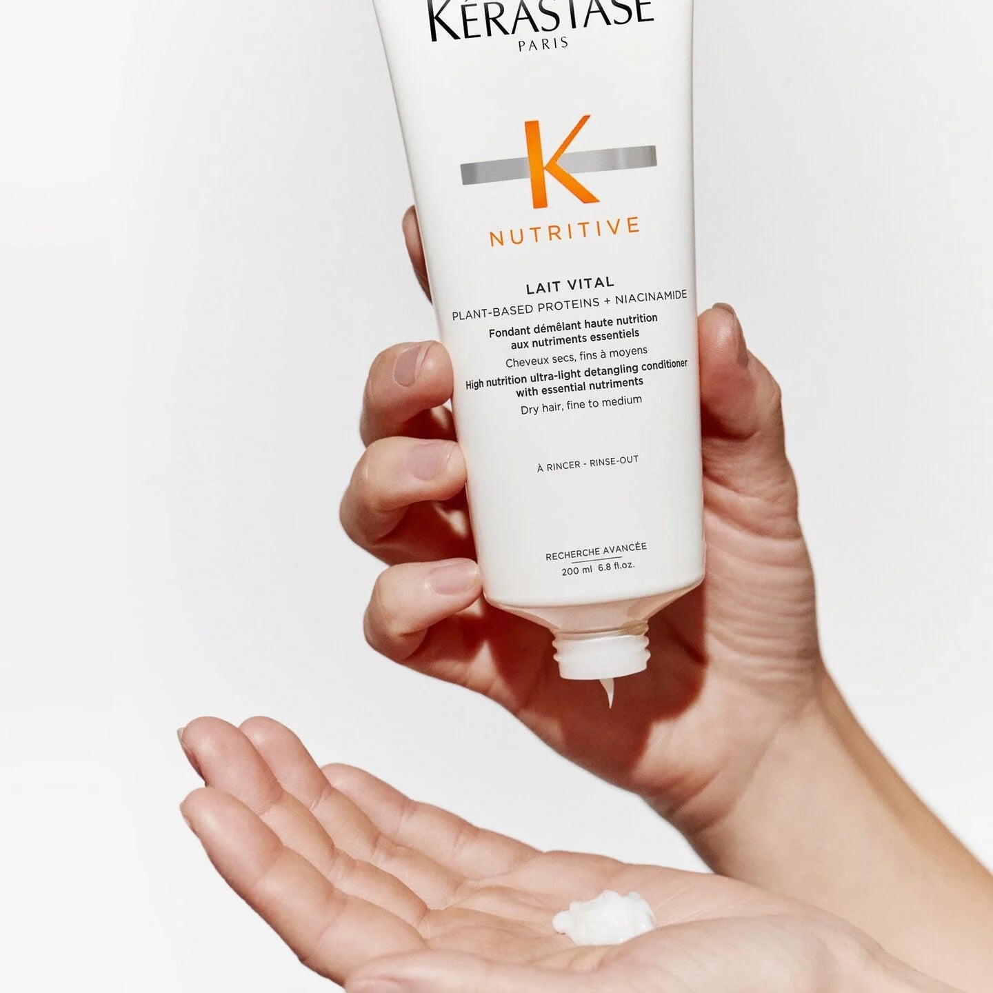 Hand holding a K?rastase Nutritive Lait Vital conditioner bottle with a small amount of product on the palm. Canada
