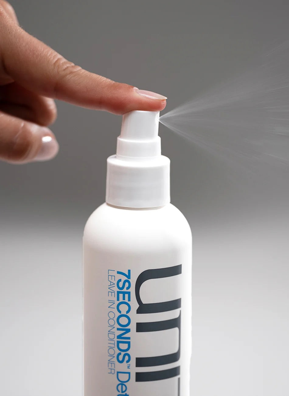 Hand holding a white spray bottle labeled '7SECONDS' with a gray background