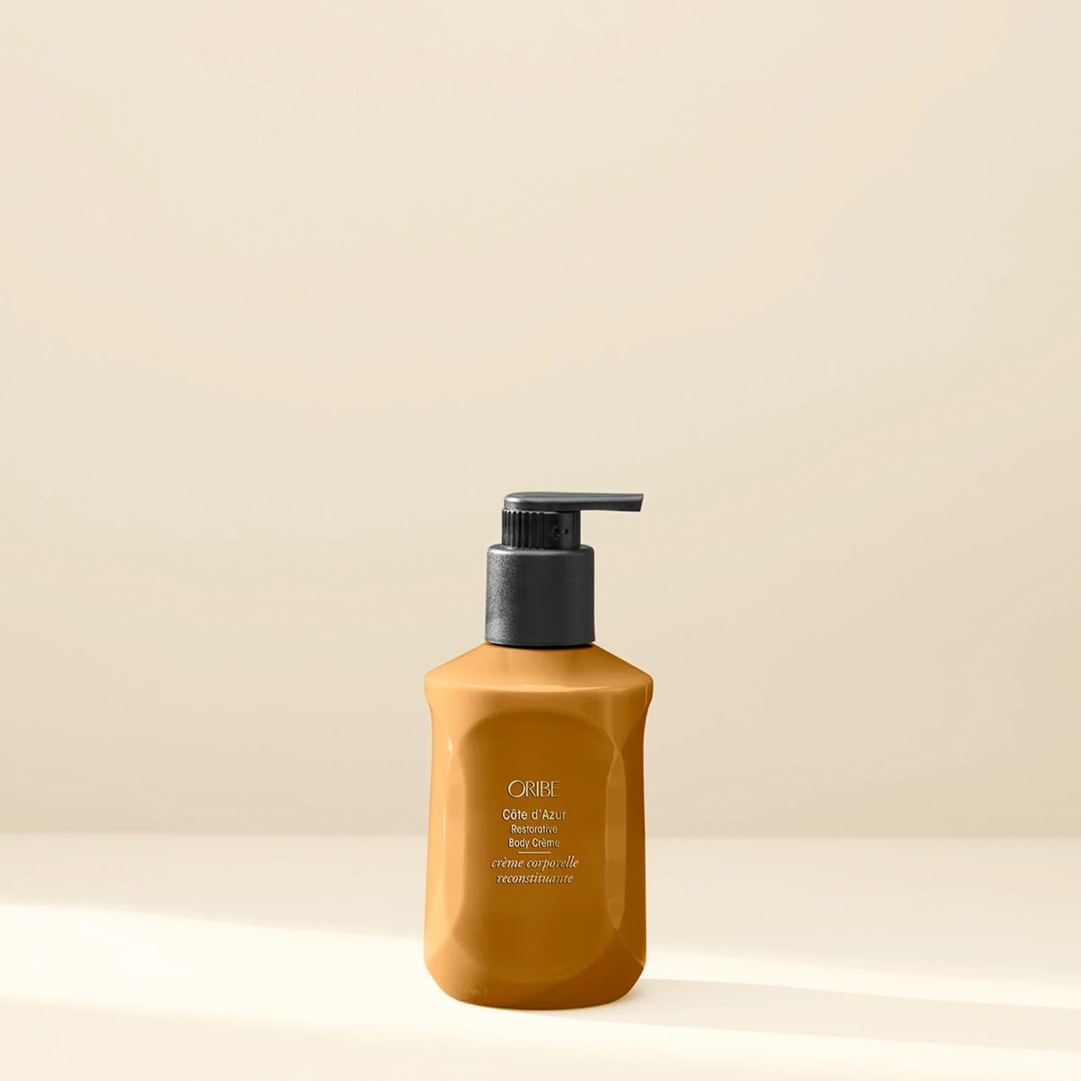 A bottle of Caviar Gold & Silk Hair Growth Serum in a warm amber-brown bottle with a black pump dispenser, set against a minimalist beige background.at Curious Salons