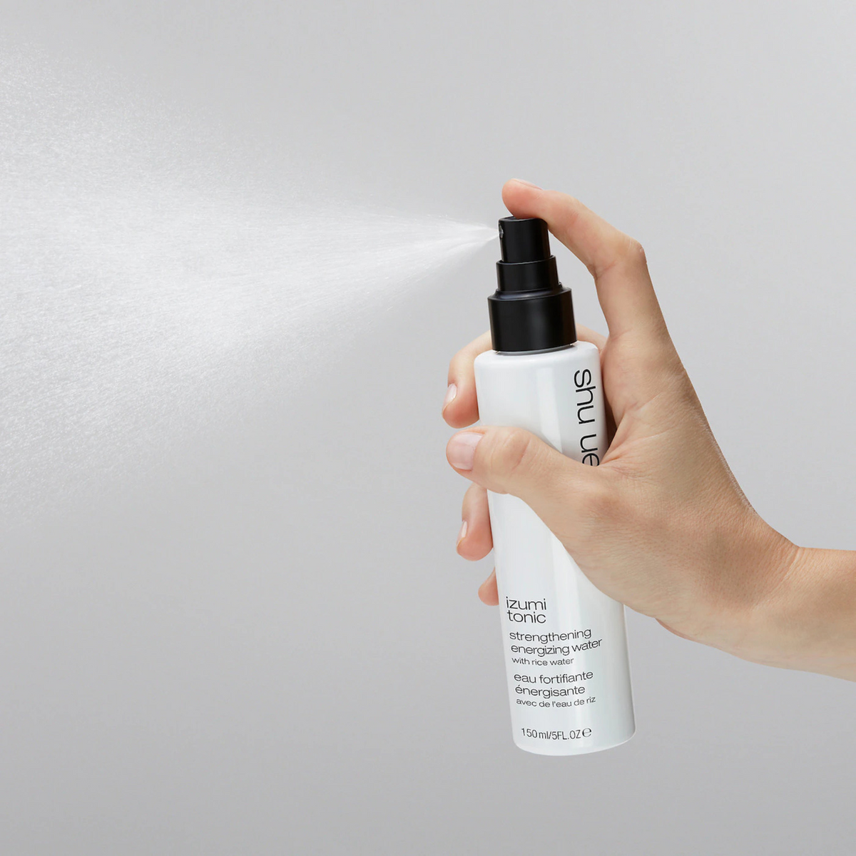 Hand holding a Shu Uemura hair product bottle against a light gray background
