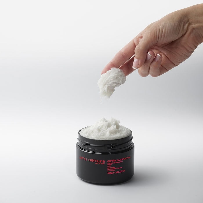 Hand scooping white cream from a black jar labeled 'mu derma' on a light gray background