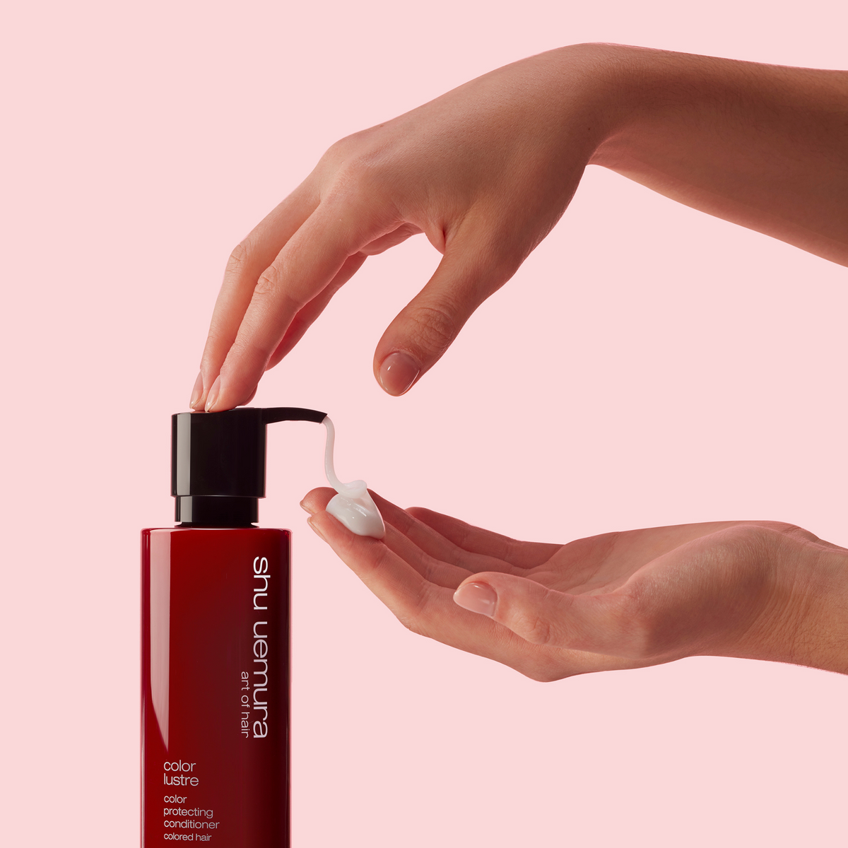 Shu Uemura hand cream being dispensed onto a hand against a pink background