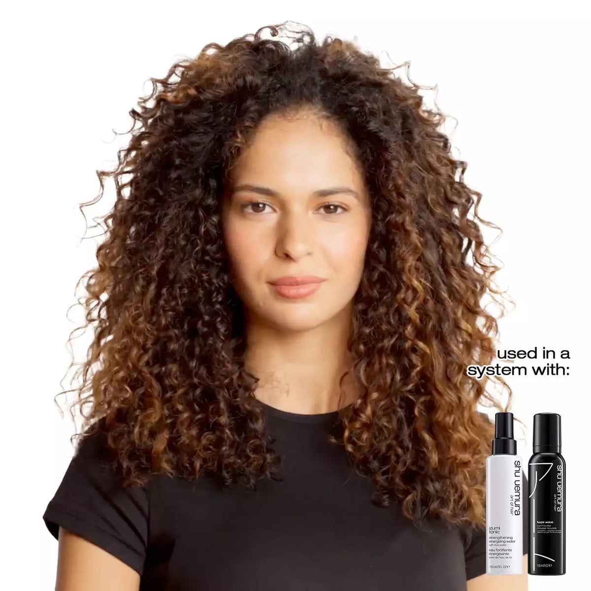 Woman with curly hair holding hair care products on a white background