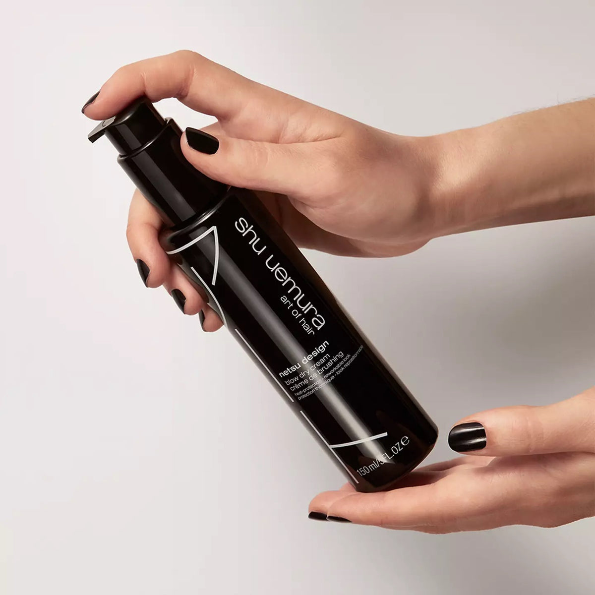 Shu Uemura hair product held by a hand against a neutral background