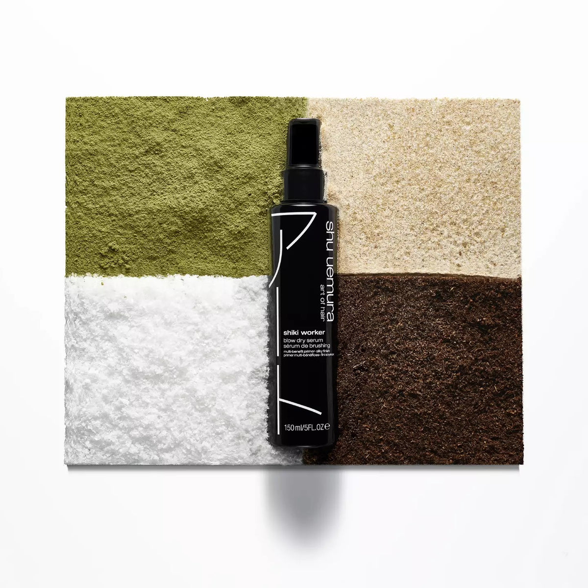Black spray bottle labeled 'Aveda' on a textured surface with green, white, and brown colors.