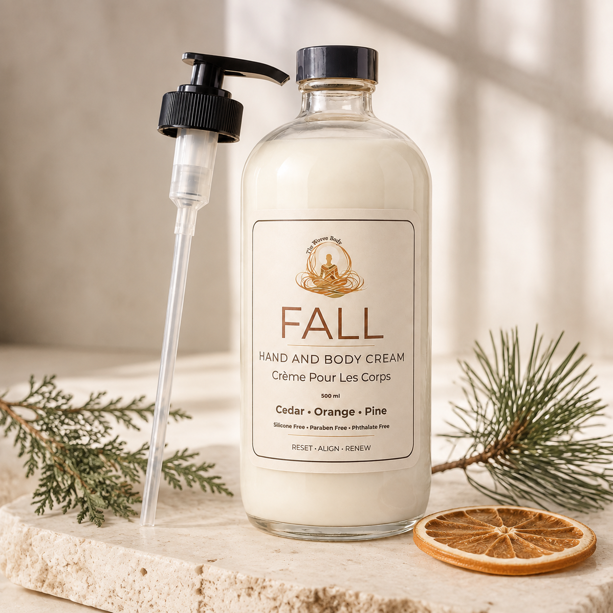 A clear glass pump bottle of Fall Hand and Body Cream stands on a stone surface with evergreen branches and a dried orange slice around it. The Woven Body FALL Body Lotion in Cedarwood, Orange & Pine — 250mL glass pump bottle, made in Calgary, Alberta"