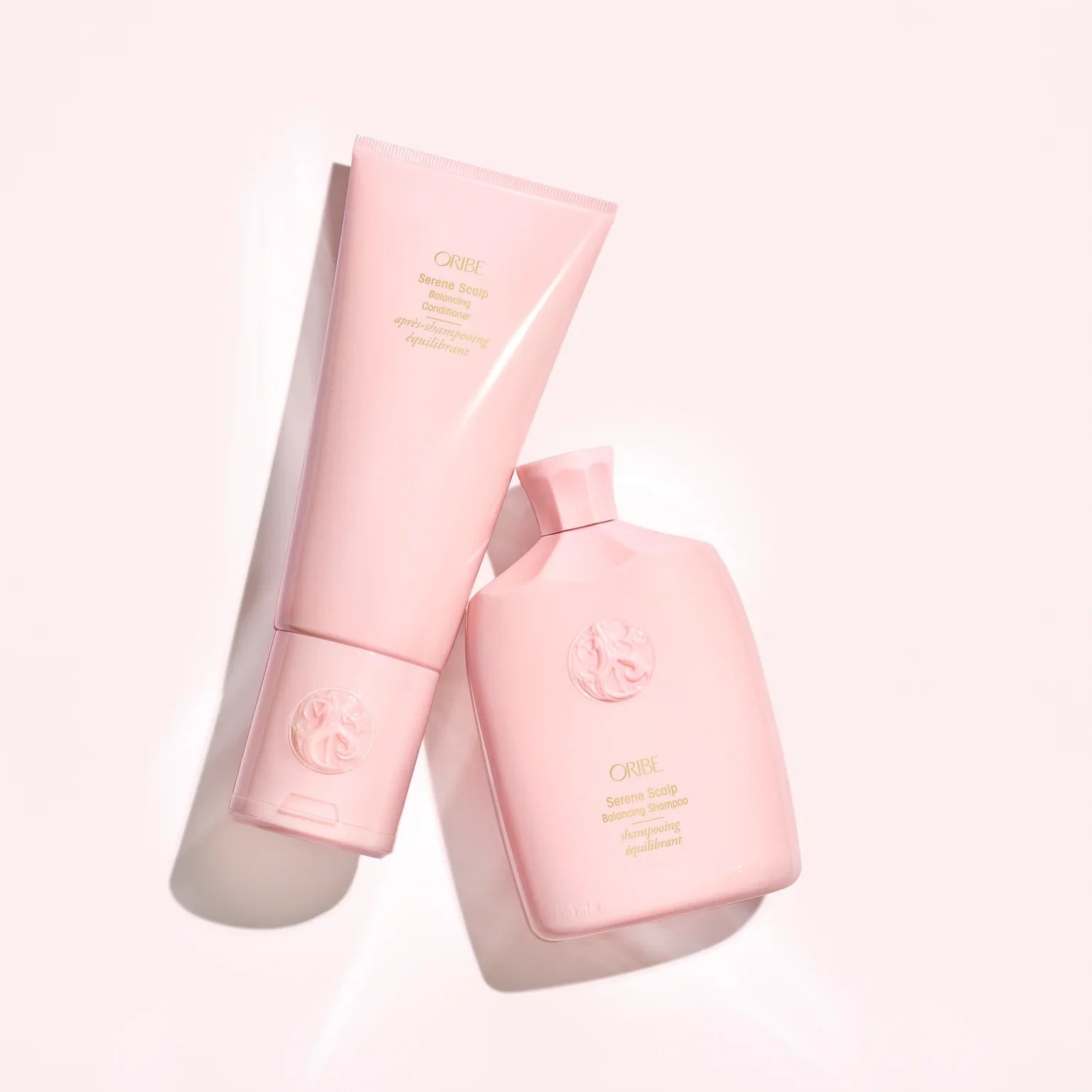 Two pink bottles with a brand logo on a light pink background Oribe Serene Scalp Balancing Shampoo for dry flaky scalp care in Canada